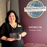 woman sranding by Toastmasters sign and holding a glass trophy